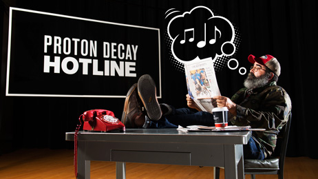 Proton decay hotline, man sits at desk with old red dial phone on desk and musical notes coming out of his mouth