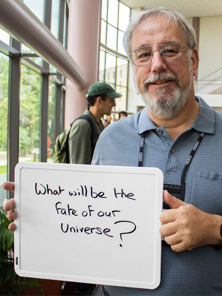 Photo of Steve Wimpenny holding whiteboard that says "What will be the fate of the universe?"