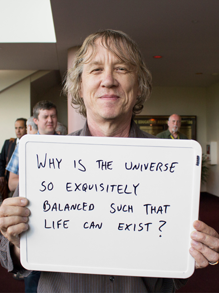 Photo of Erik Ramberg holding whiteboard that says "Why is the universe so exquisitely balanced such that life can exist?"