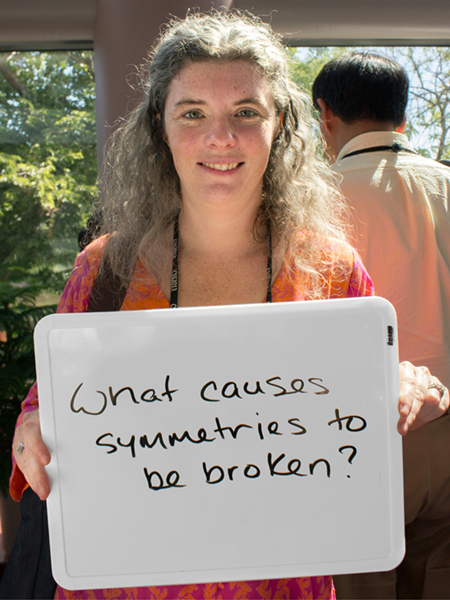 Photo of Elizabeth Worcester holding whiteboard that says "What causes symmetries be broken?"