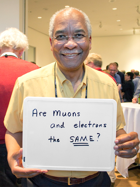 Photo of Herman White holding whiteboard that says "Are muons and electrons the same?"