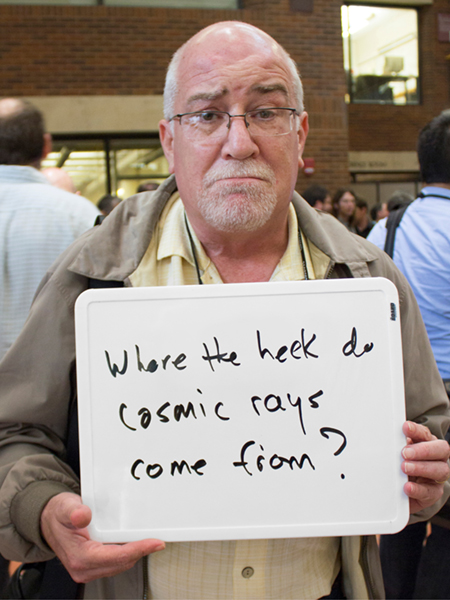 Photo of James Matthews holding whiteboard that says "Where the heck do cosmic rays come from?"