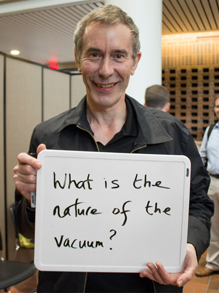 Photo of Ian Shipsey holding whiteboard that says "What is the nature of the vacuum?"