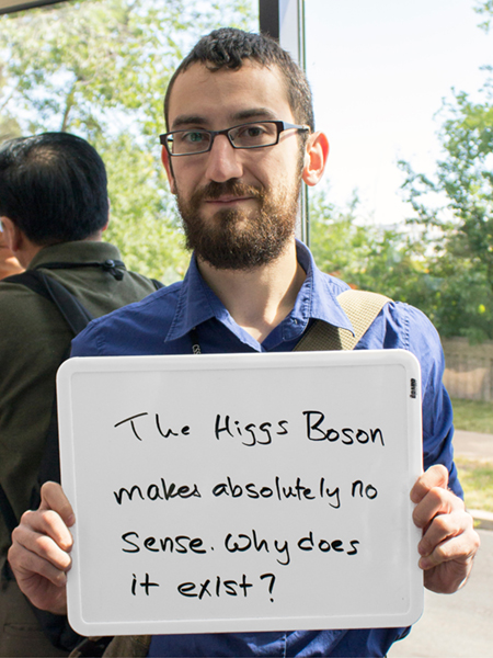 Photo of Richard Ruiz holding a whiteboard that says "The Higgs Boson makes absolutely no sense. Why does it exist?"