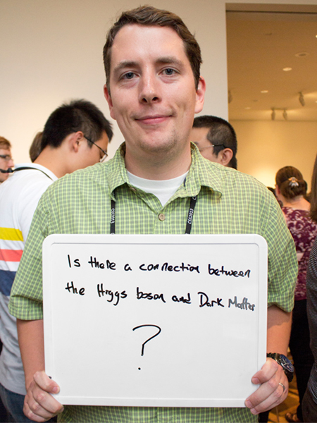Photo of Gabe Shaughnessy holding whiteboard that says "Is there a connection between the Higgs boson and Dark Matter?"