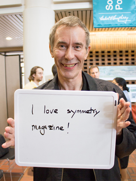 Photo of man holding a whiteboard that says "I love symmetry magazine"