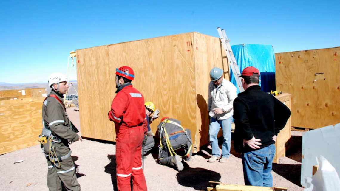 Photo of men on Dark Energy Camera site working on wooden crates in helmets and protective suits