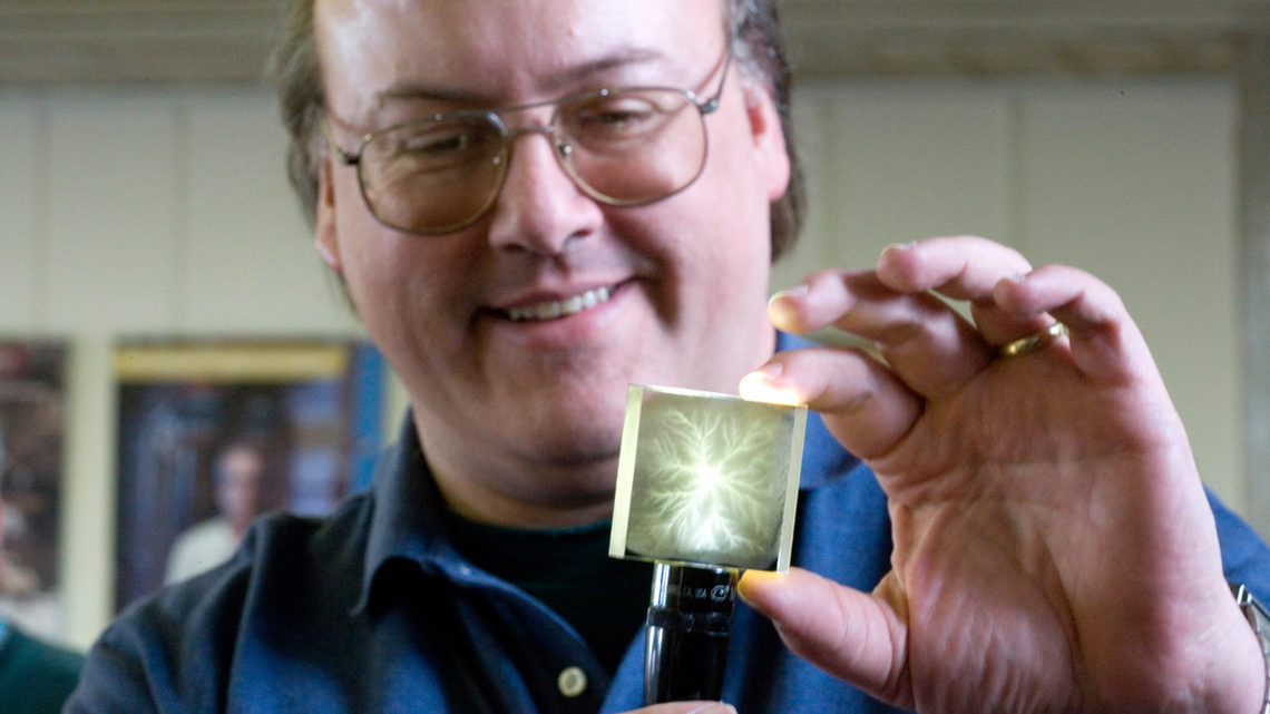 Photo of artist Todd Johnson illuminates the electron trails in a small block of acrylic