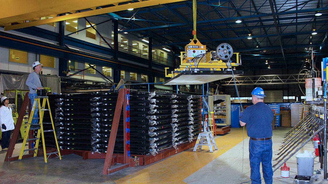In the assembly building, technicians guide a vacuum suction lifter carrying a plastic module