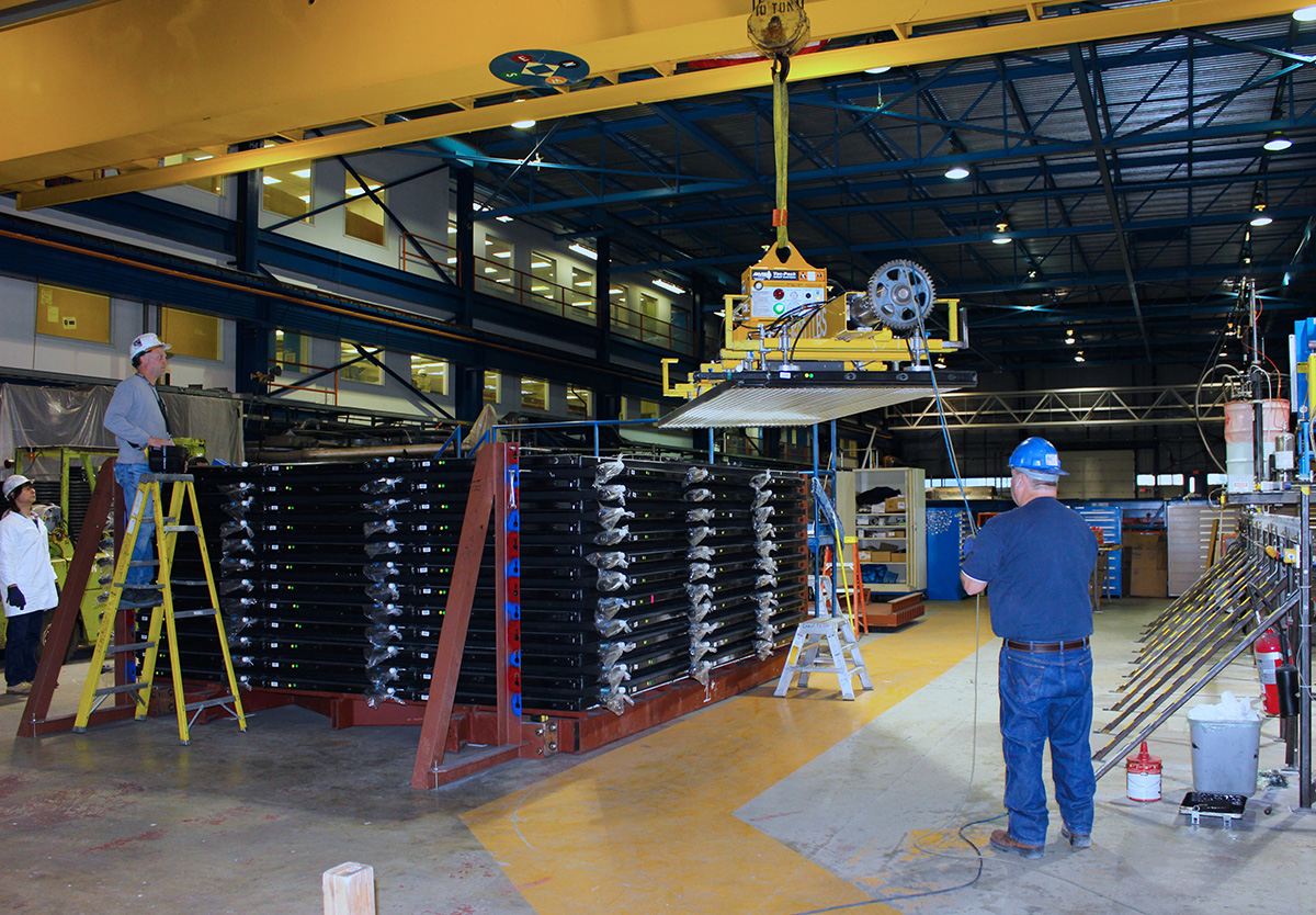 In the assembly building, technicians guide a vacuum suction lifter carrying a plastic module