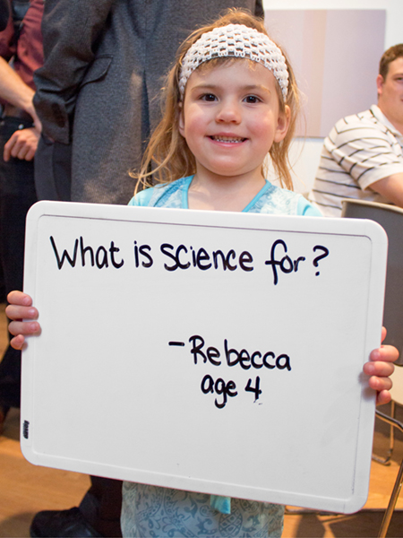 Photo of girl holding a whiteboard that says "What is science for?"