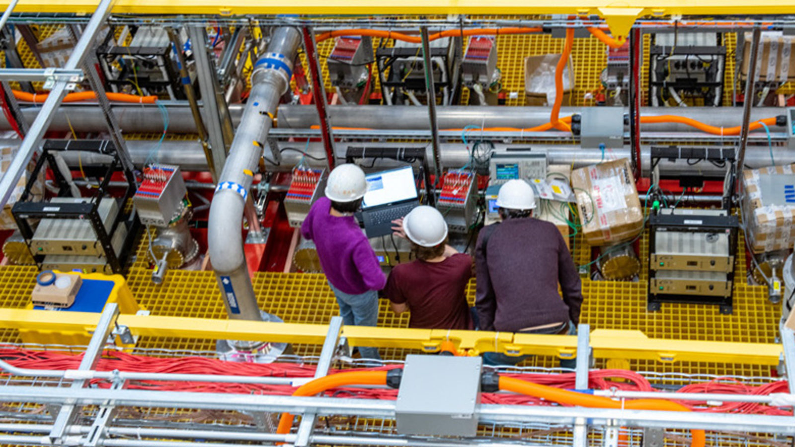 Three scientists in white hard hats working on the ICARUS detector, photographed from above.