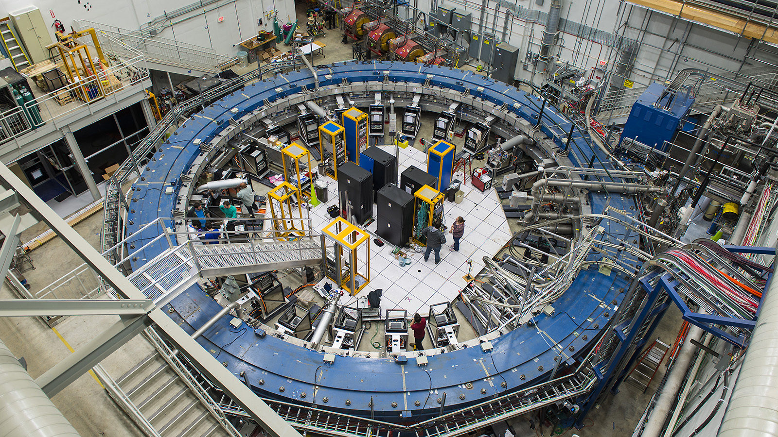 Overhead view of people working inside a room-sized blue ring, the Muon g-2 magnet
