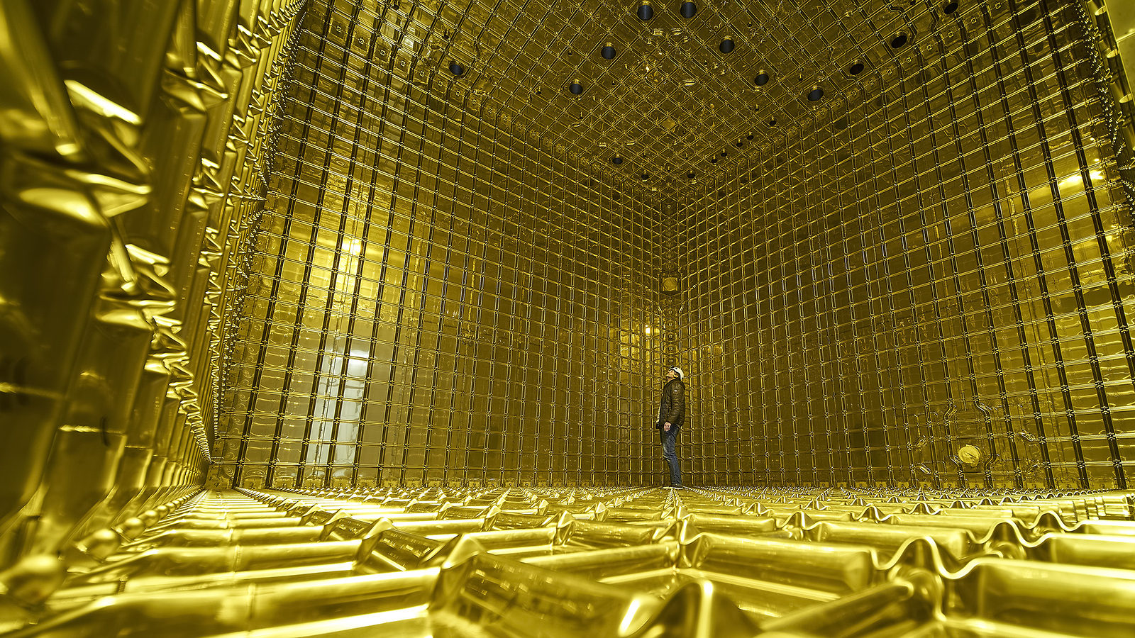 Photo of a person standing inside the ProtoDUNE detector, the walls, floor, and ceiling are all yellow