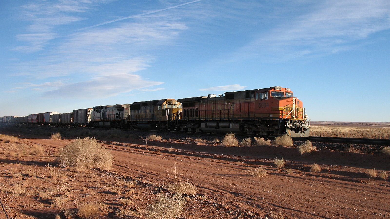 Photo of a train traveling along tracks out in the desert 