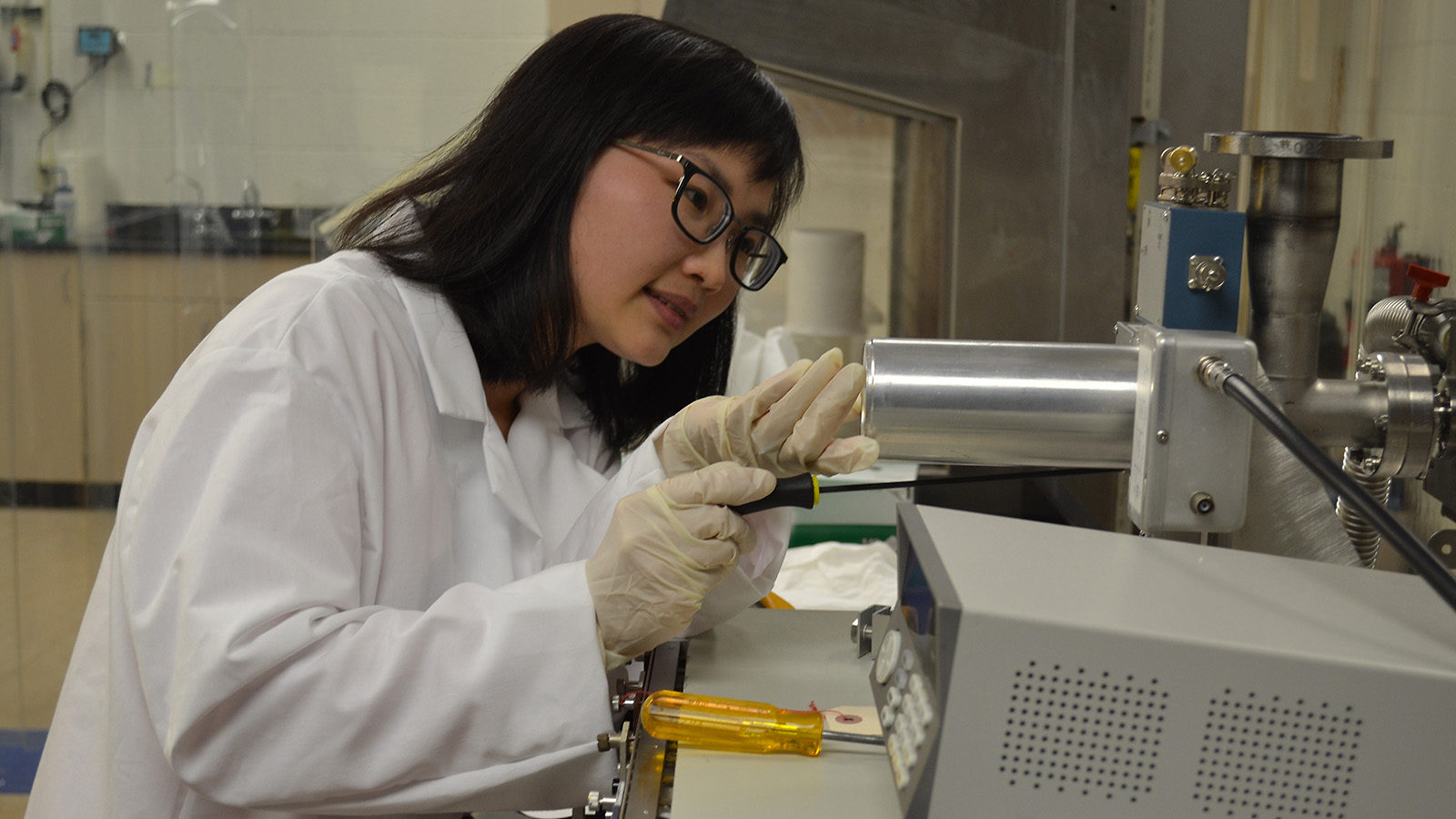 Photo of Wenzhao Wei, dressed in a white coat and gloves, working in a lab