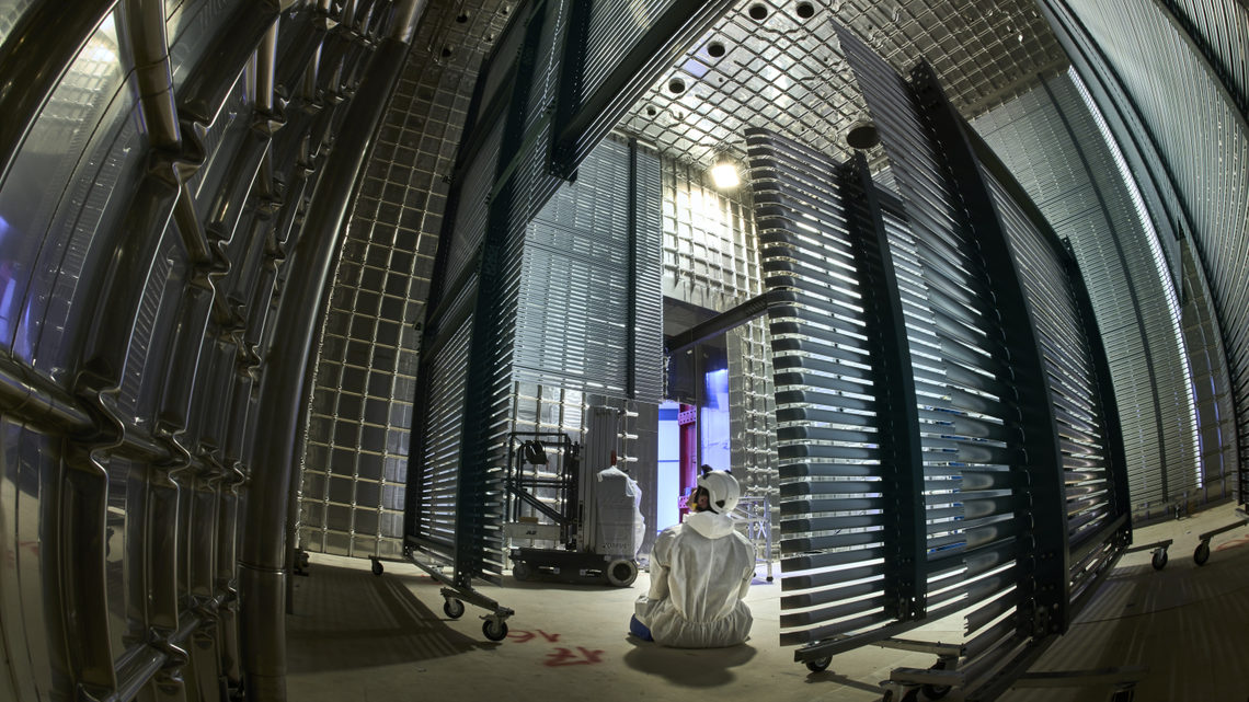 A person in cleanroom garb sits inside the ProtoDUNE detector.