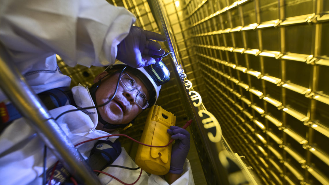 A person in a clean suit examines components of ProtoDUNE