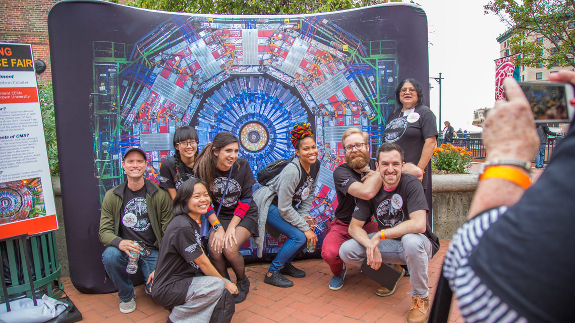 Group of scientists, professors, and volunteers posing in front a Big Bang Science Fair backdrop