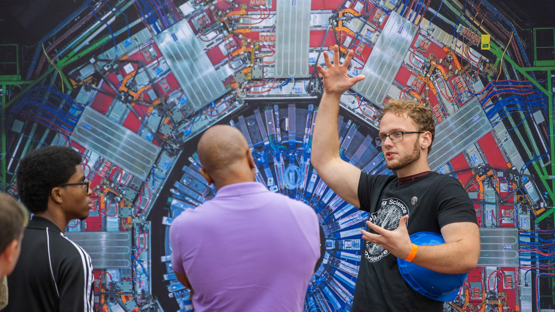 A volunteer explains the CMS experiment in front of an image of the CMS detector