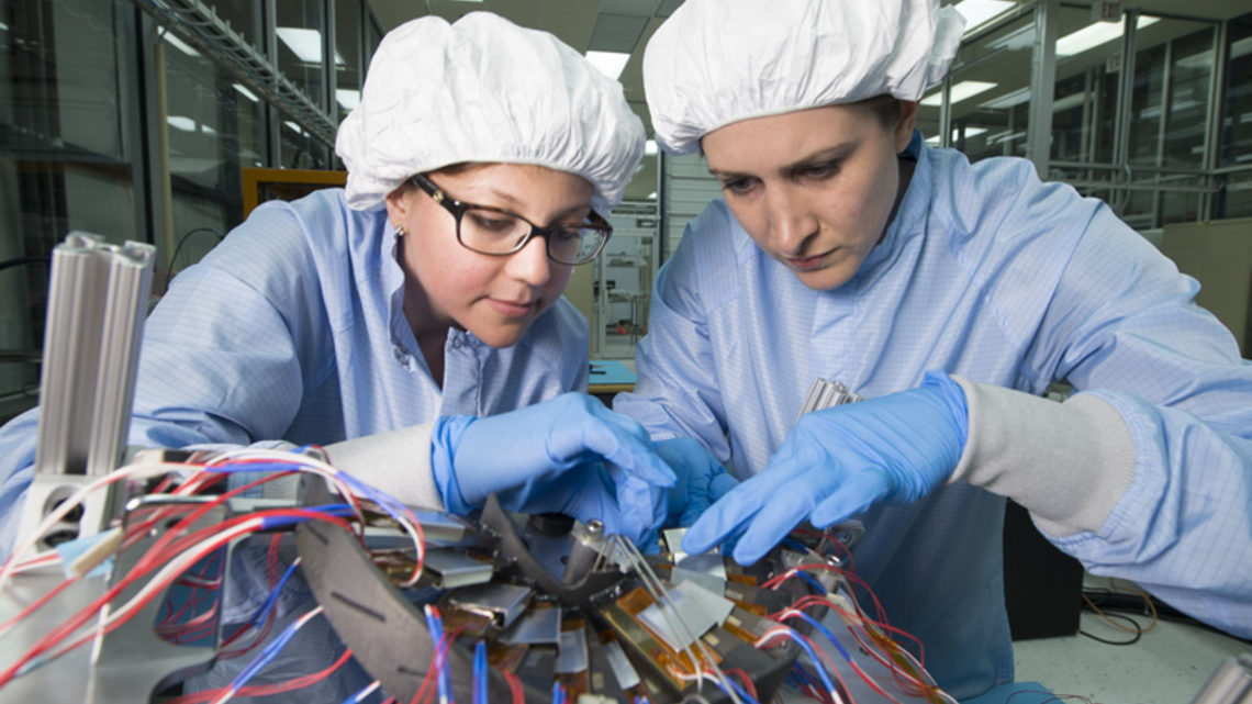 Scientists Maral Alyari and Stephanie Timpone, wearing clean room gear, inspect the detector.