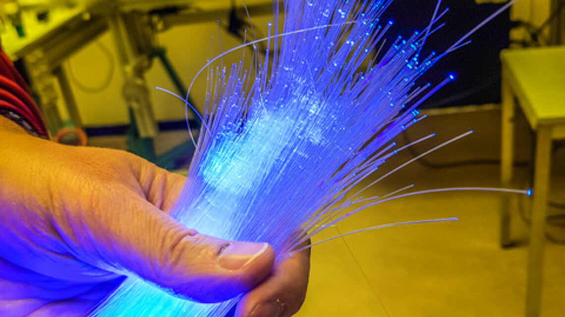 Photo of a hand holding glowing blue optical fibers