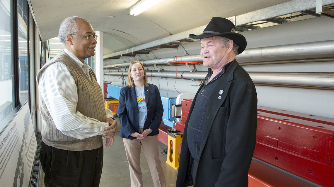 Monkee Micky Dolenz stands by a model particle accelerator with two Fermilab employees