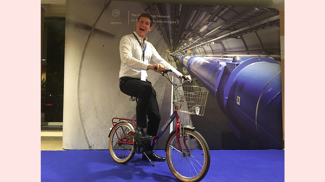 Pasner posing on a bike in front of an image of a CERN tunnel