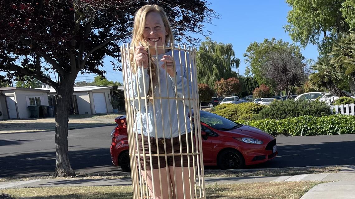 Photograph of Jannicke Pearkes outside in a neighborhood, standing inside the largest wooden cylinder of the Disco-tracker
