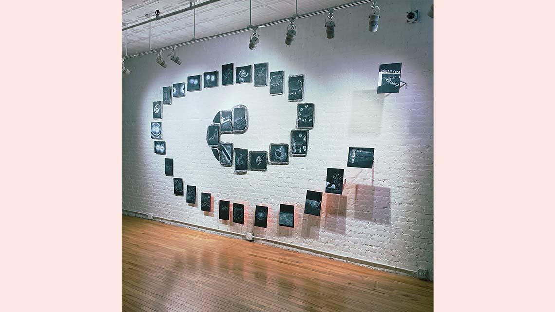 photograph of images with black backgrounds arranged on a white gallery wall in the shape of a spiral
