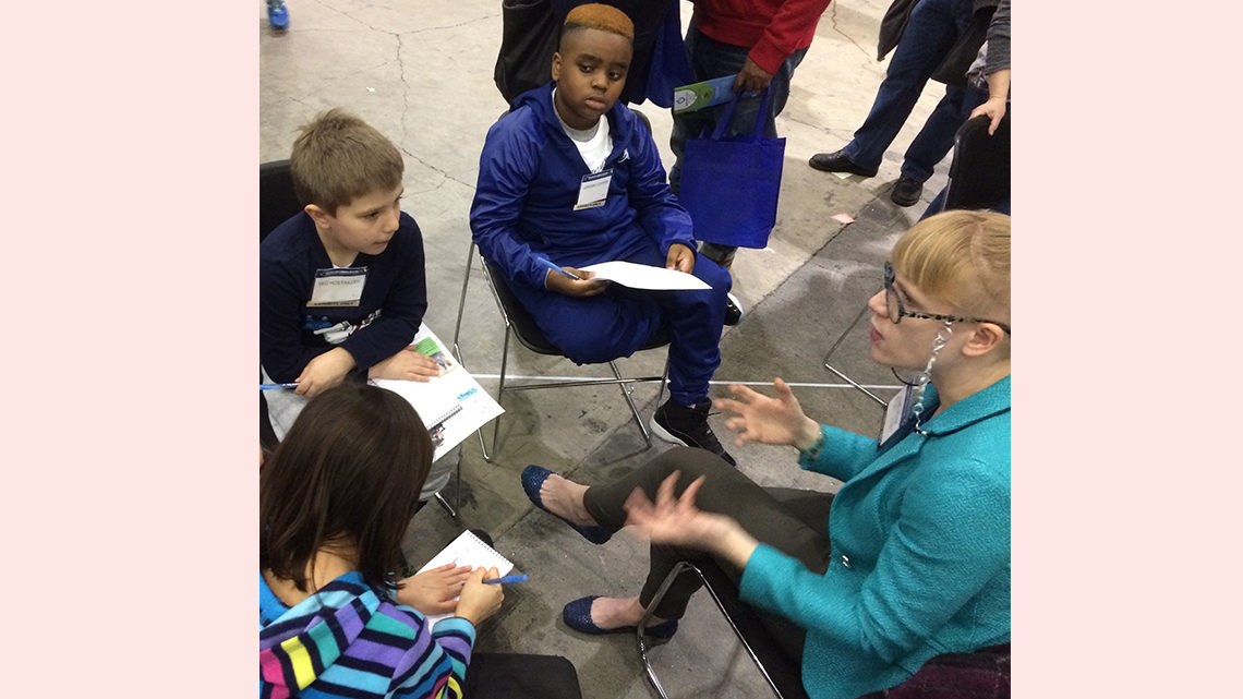 Children sitting around a scientist interviewing