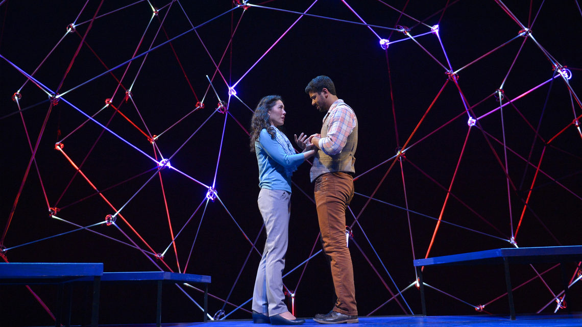 A scene from Constellations: a man and woman on stage holding hands