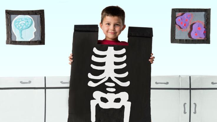 Photo of child holding a cut-out of an X-ray of his skeleton over his body 