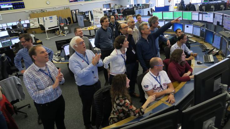 Photo accelerator operators and CERN's Director General stand together watching the process of the LHC beam on a computer screen